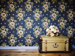 나무 floor 안의 앞 floral wallpaper 위에 앉아 있는 suitcase