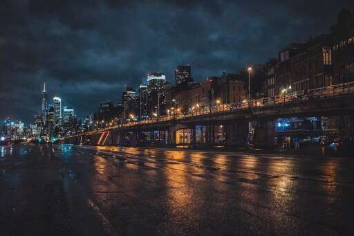 nighttime view of a city street with a bridge and buildings in the background