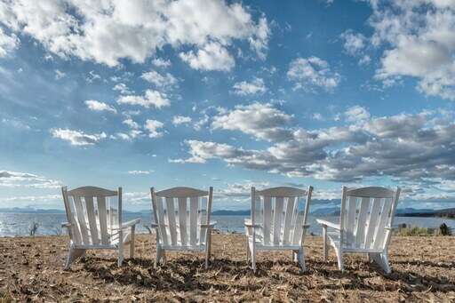 there are three white chairs sitting in the sand near the water